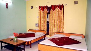 A room with two single beds, a small table with a vase of flowers, and a wardrobe in the background. - Hotel Golden (Haridwar)