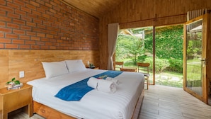 A bedroom with a wooden headboard, a large bed with white bedding, a blue throw, and a view of a garden through a sliding glass door. - Dendi Resort Phu Quoc (Phu Quoc)