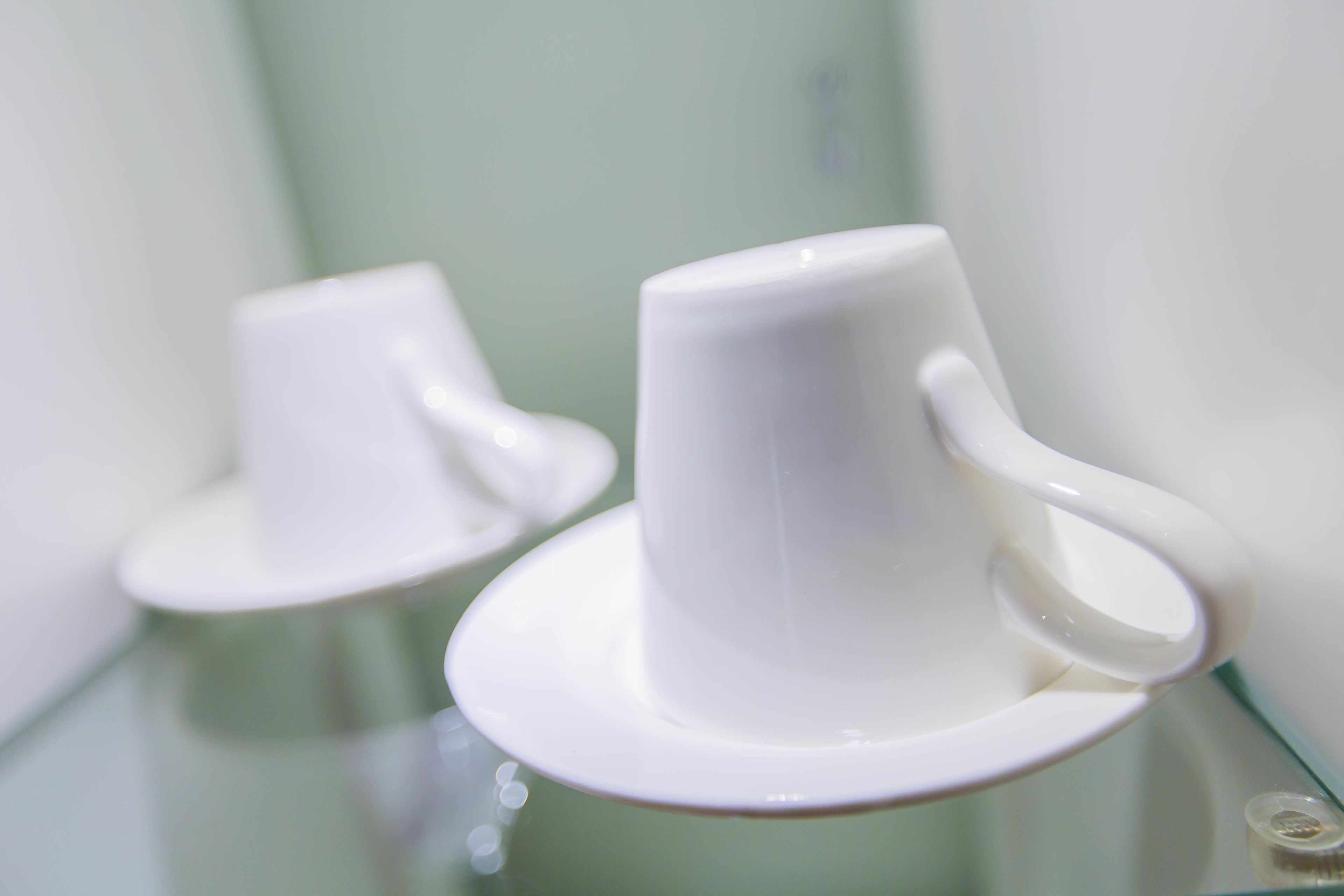 Two white ceramic cups on a glass table.