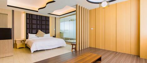 A modern hotel room with a large bed, wooden flooring, a built-in bench, a TV, and a unique ceiling design.
