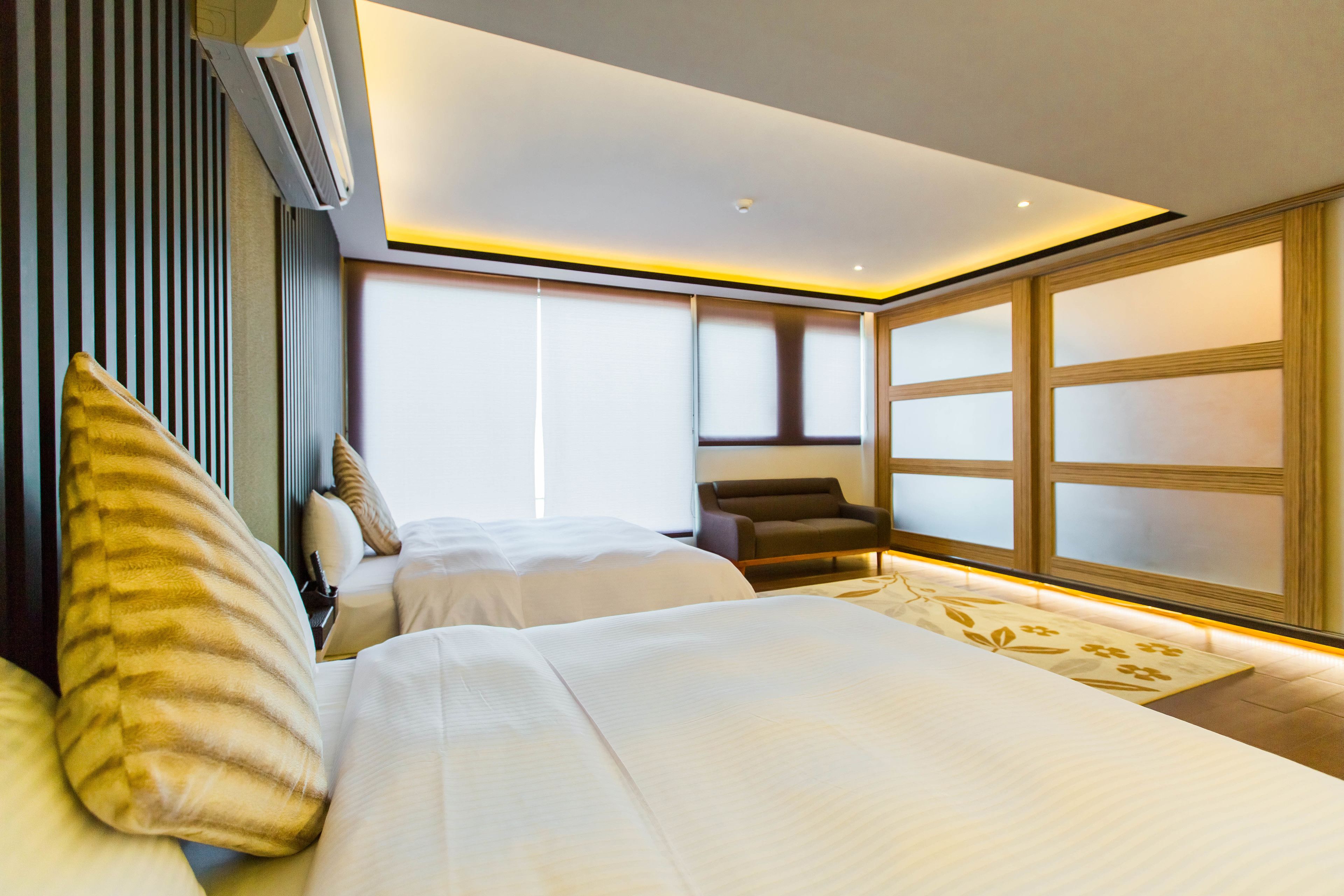 Una habitación de hotel moderna con dos camas, una zona de estar y ventanas grandes.