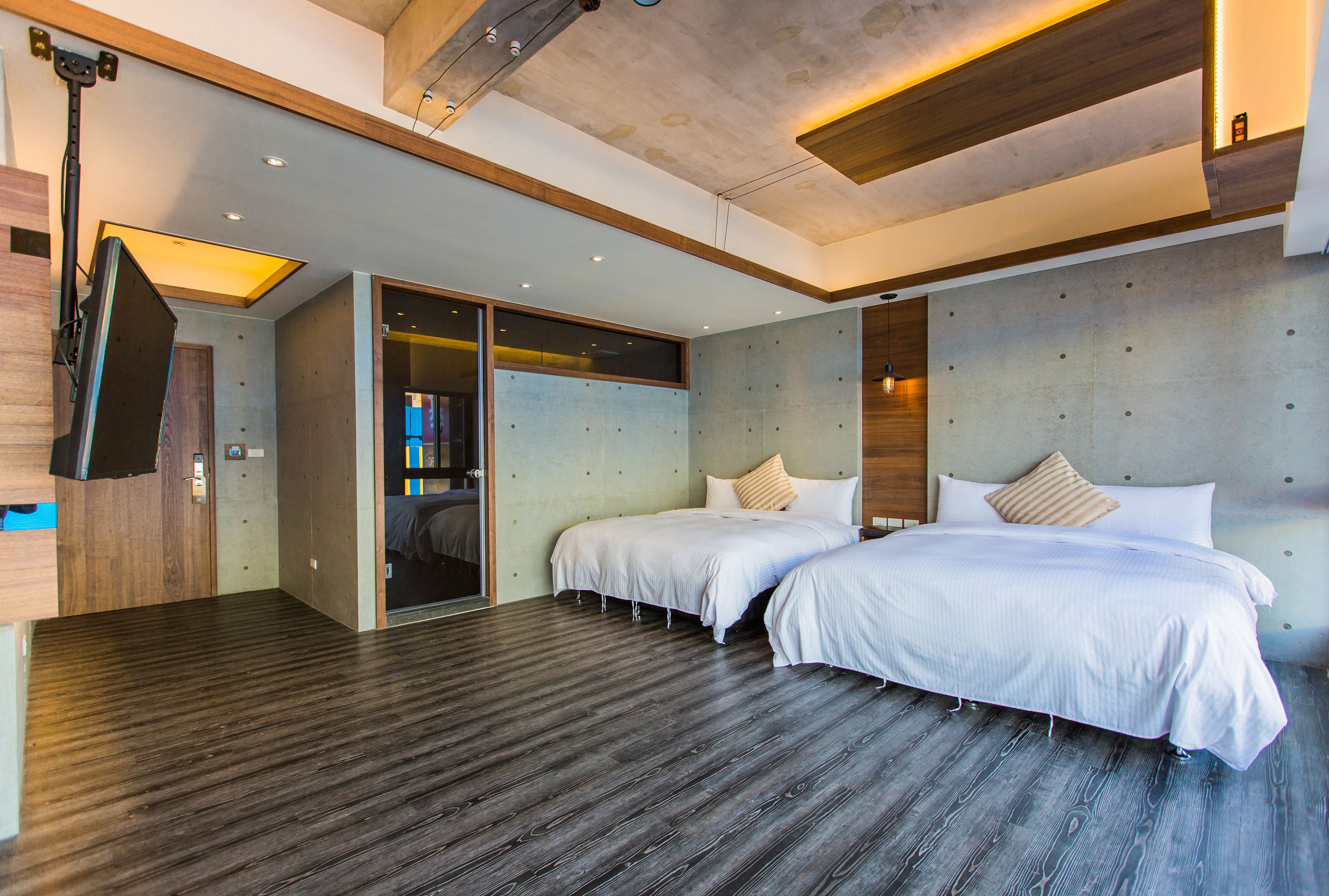 Een moderne hotelkamer met twee bedden, een houten vloer en een schuifdeur naar de badkamer.