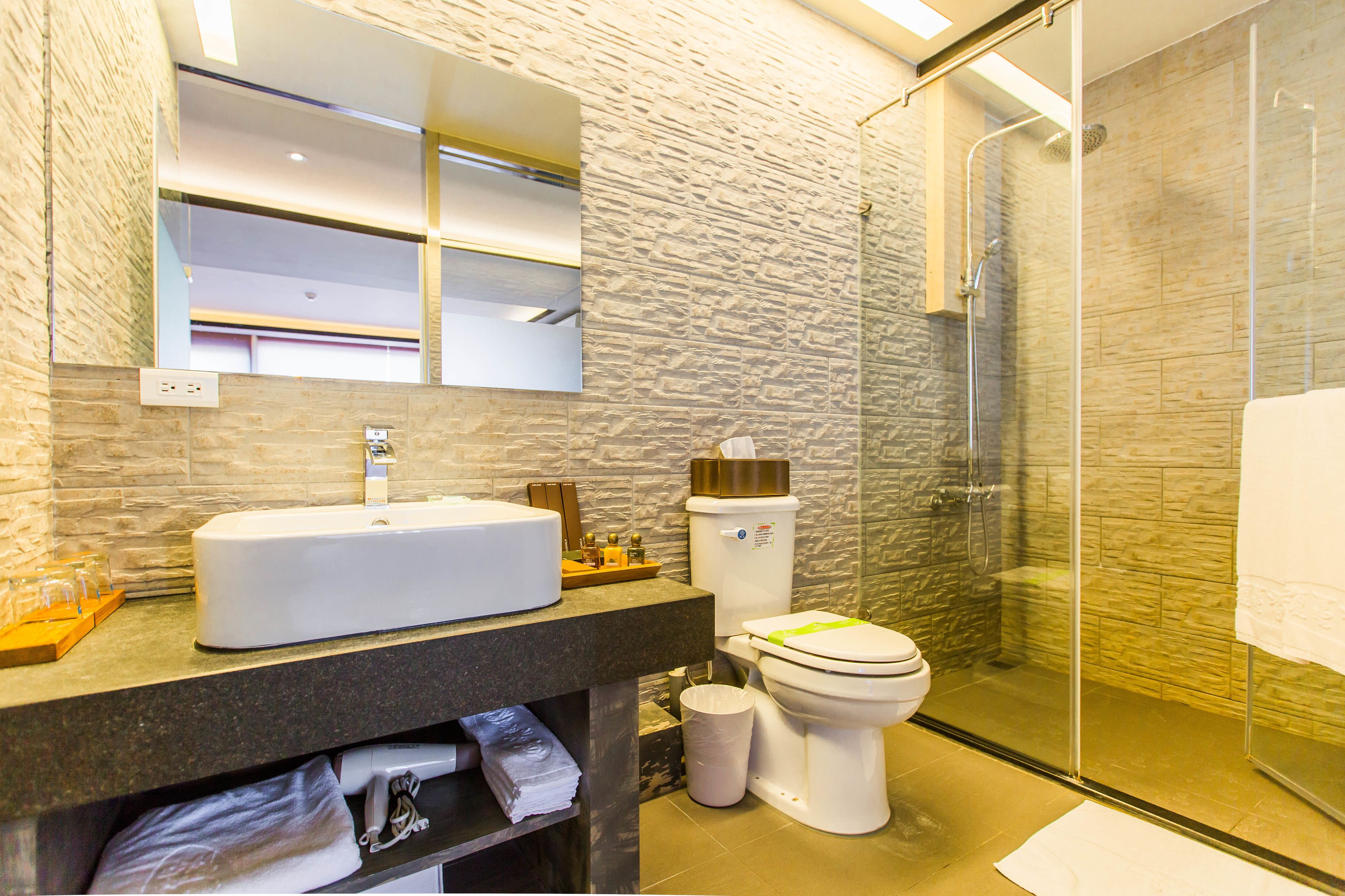 Een moderne badkamer met een wand met een steenstructuur, een groot wit wastafelmeubel, een toilet en een douchecabine met glazen wanden.