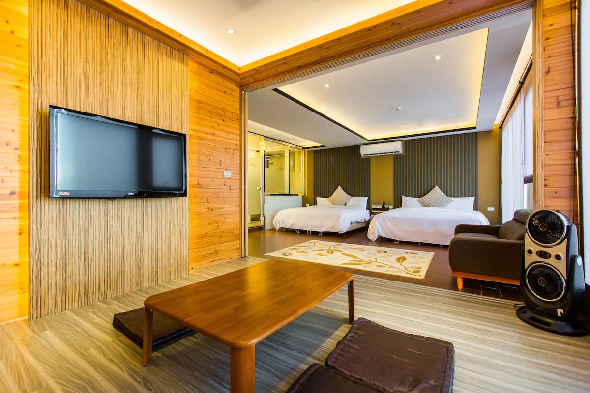 A modern hotel room with a wooden wall, a flat-screen TV, a bed, a sofa, and a coffee table.