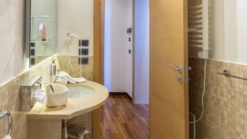 A bathroom with a sink, mirror, towel rack, and shower area.