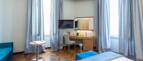 Ein Hotelzimmer mit Bett, Schreibtisch, Stuhl, Fernseher und kleinem Tisch.