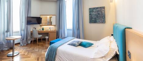 A hotel room with a bed, a desk, a chair, a TV, and a painting on the wall.