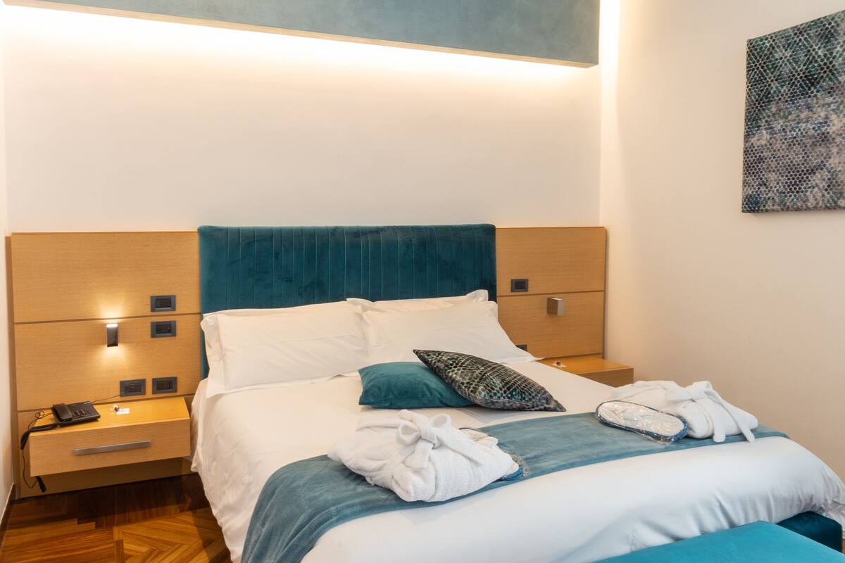 Une chambre à coucher moderne avec un grand lit, deux tables de chevet, une tête de lit et une œuvre d’art accrochée au mur.