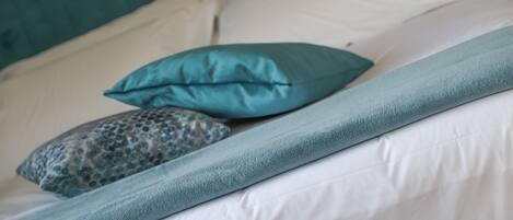 A bed with a teal bedspread, two pillows, and a patterned pillow.