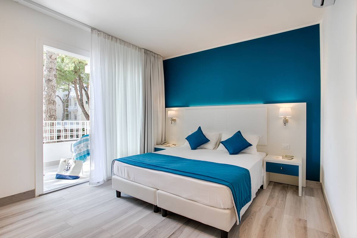 Una habitación de hotel moderna con una cama grande, dos mesitas de noche y vistas a un balcón.