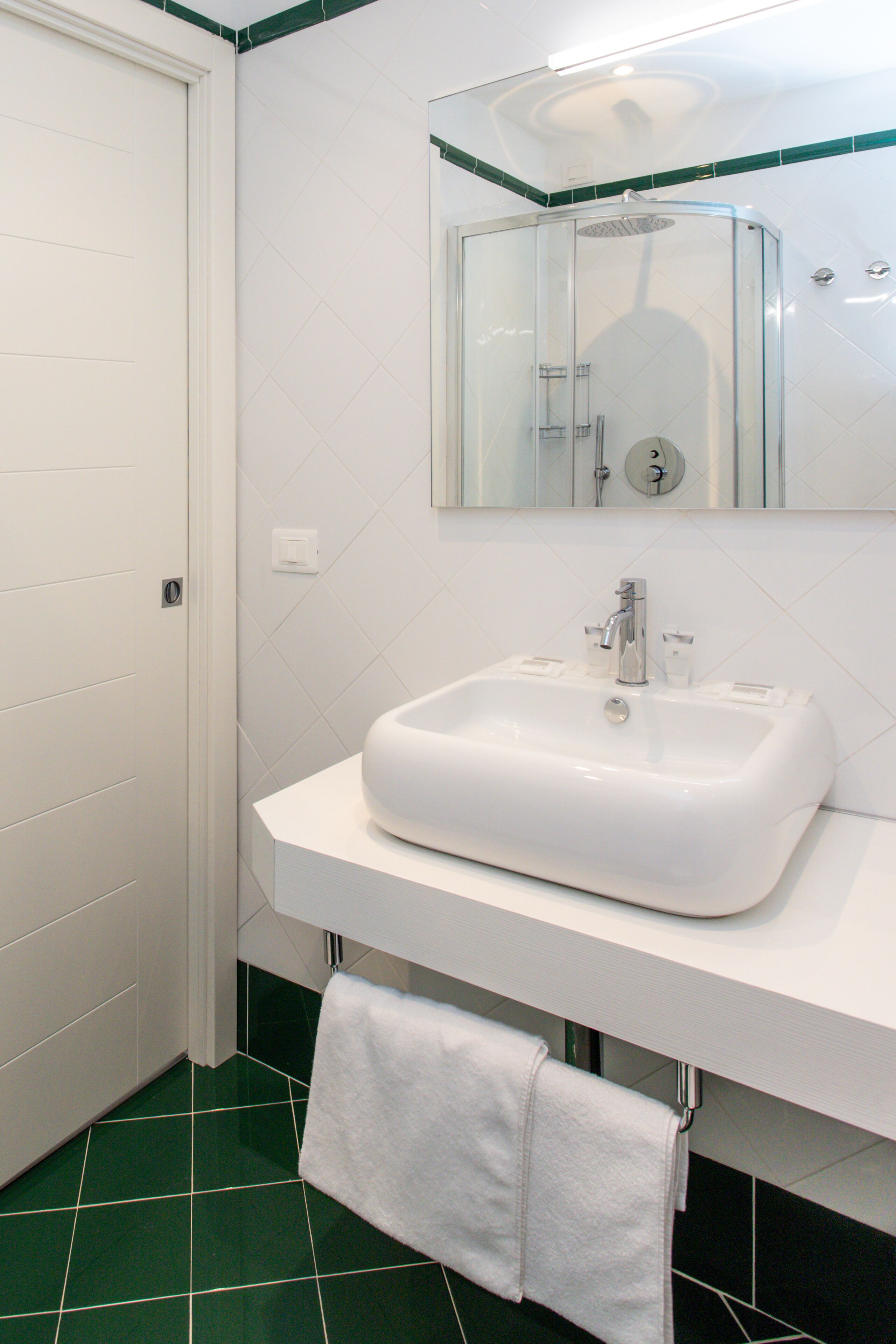 A bathroom with a white sink, a mirror, and a green-tiled floor.