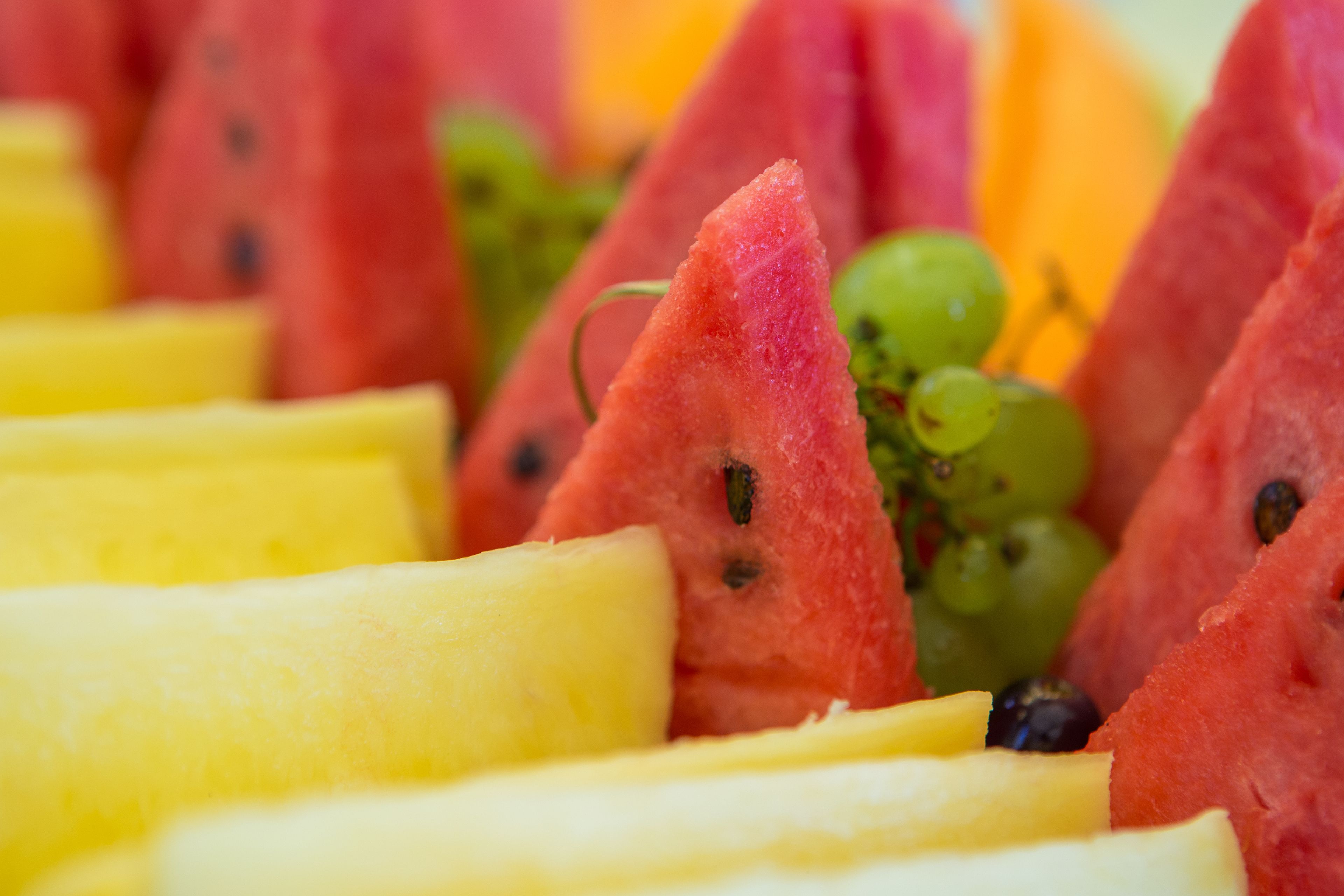Primer plano de diversas frutas, incluyendo sandía, uvas y rodajas amarillas, probablemente dispuestas para una bandeja de frutas.