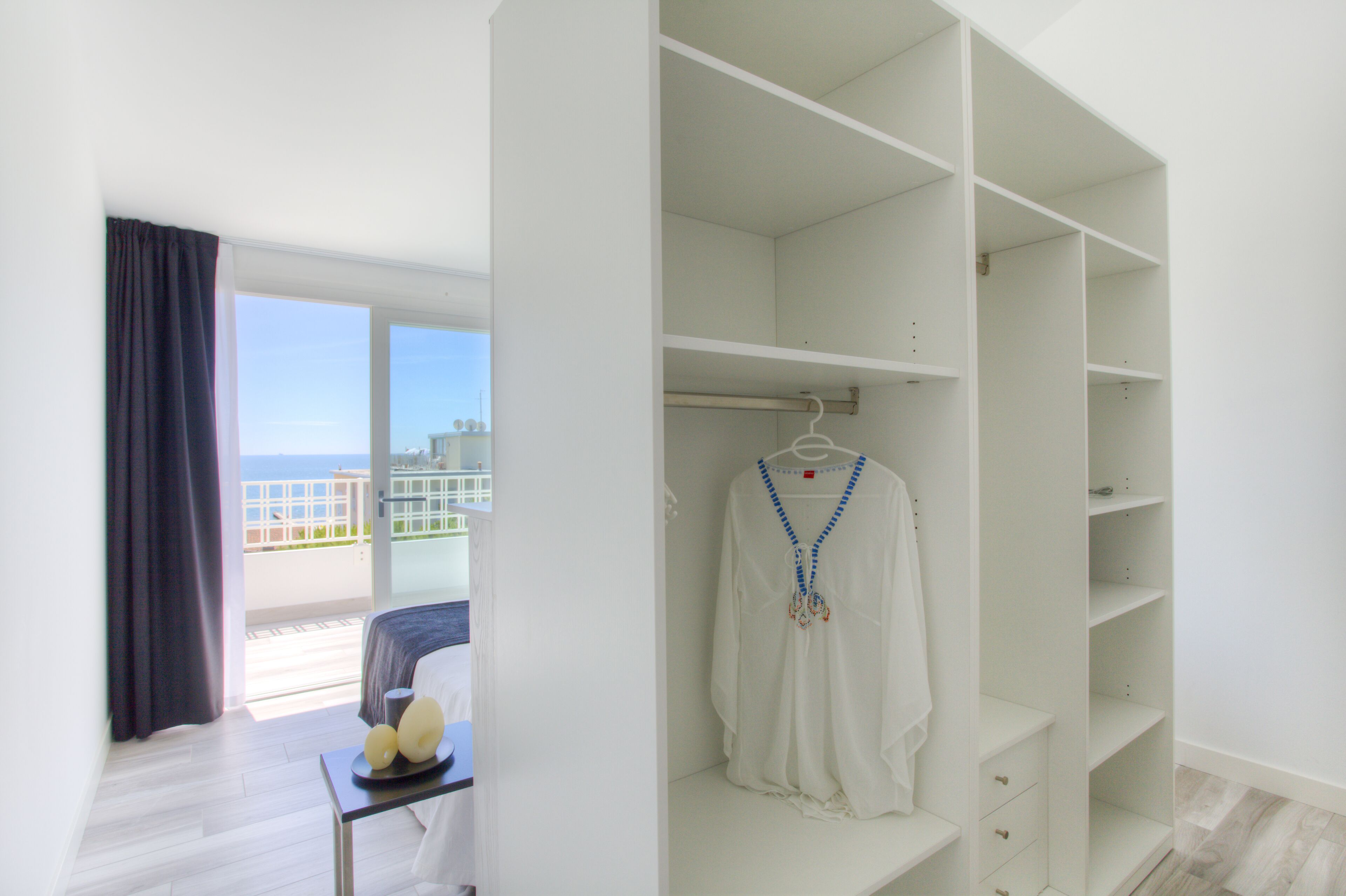 A hotel room with a balcony, a white wardrobe, and a table with decorative items.