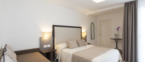 A hotel room with a bed, bedside tables, a nightstand, a lamp, a mirror, and a window with curtains.