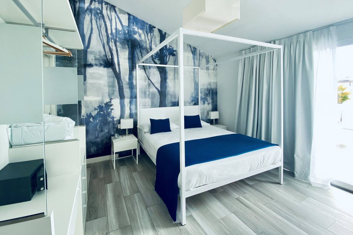Un dormitorio moderno con una cama con dosel, un amplio mural abstracto en la pared y vistas al exterior a través de la ventana.