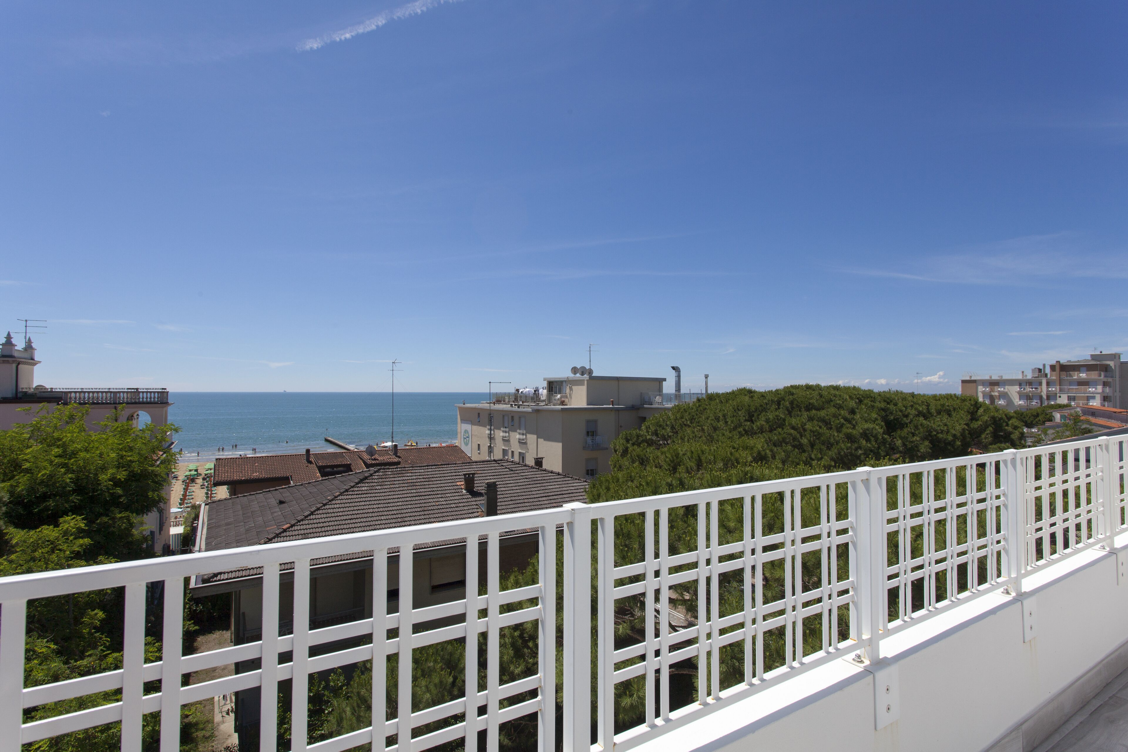 A coastal view from a balcony with a white railing, overlooking a beach and buildings.