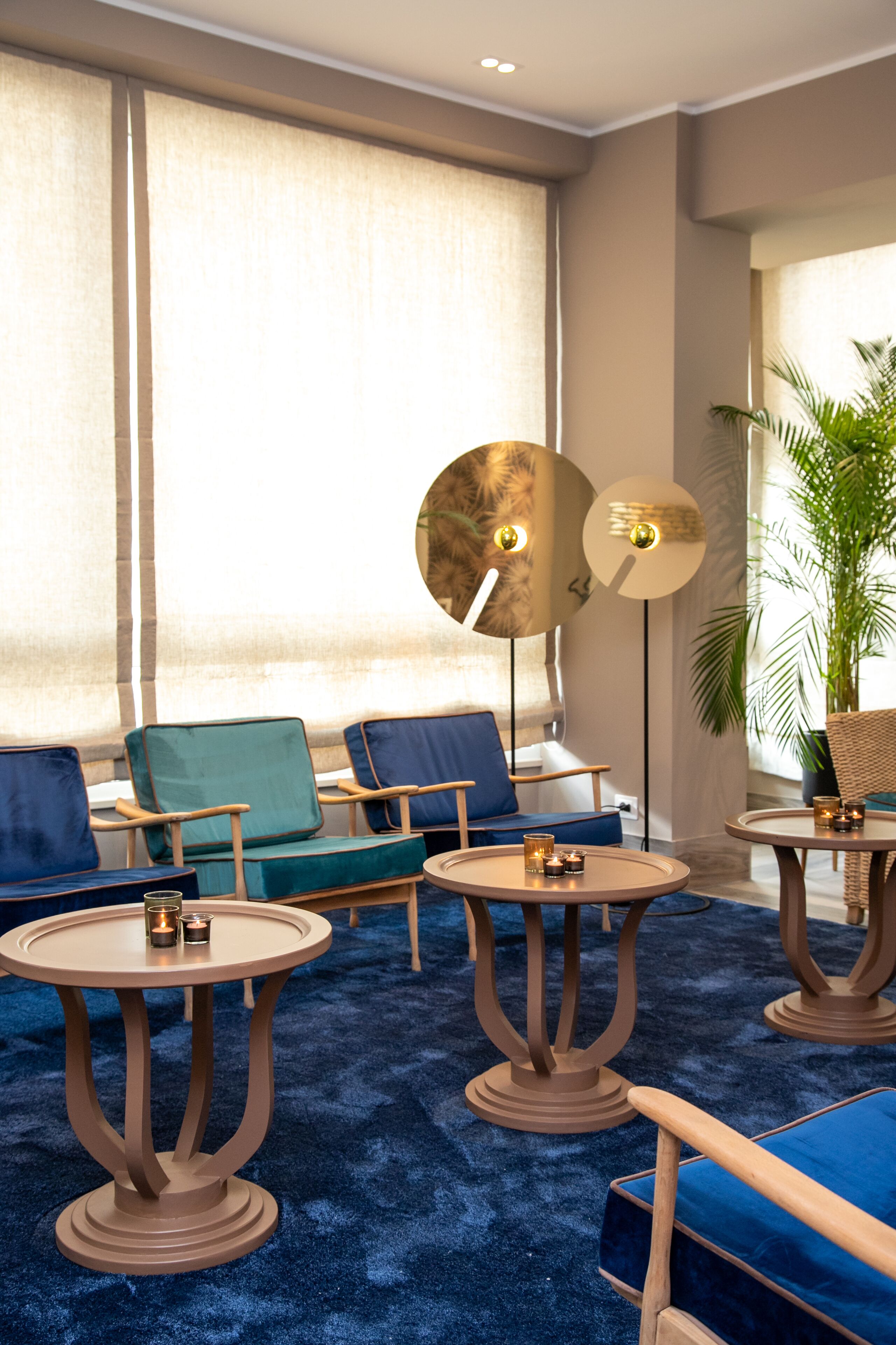 A modern lounge area with blue sofas, round tables, and a large potted plant.