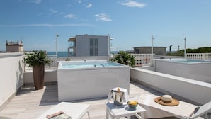 Una terraza en la azotea con jacuzzi, sillones de descanso y vistas al mar.