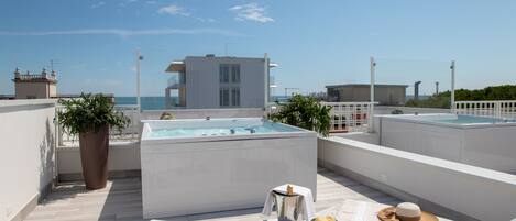A rooftop terrace with a hot tub, lounge chairs, and a view of the sea.