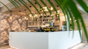 Un área de bar moderna con una isla central, suelo de madera y lámparas colgantes.