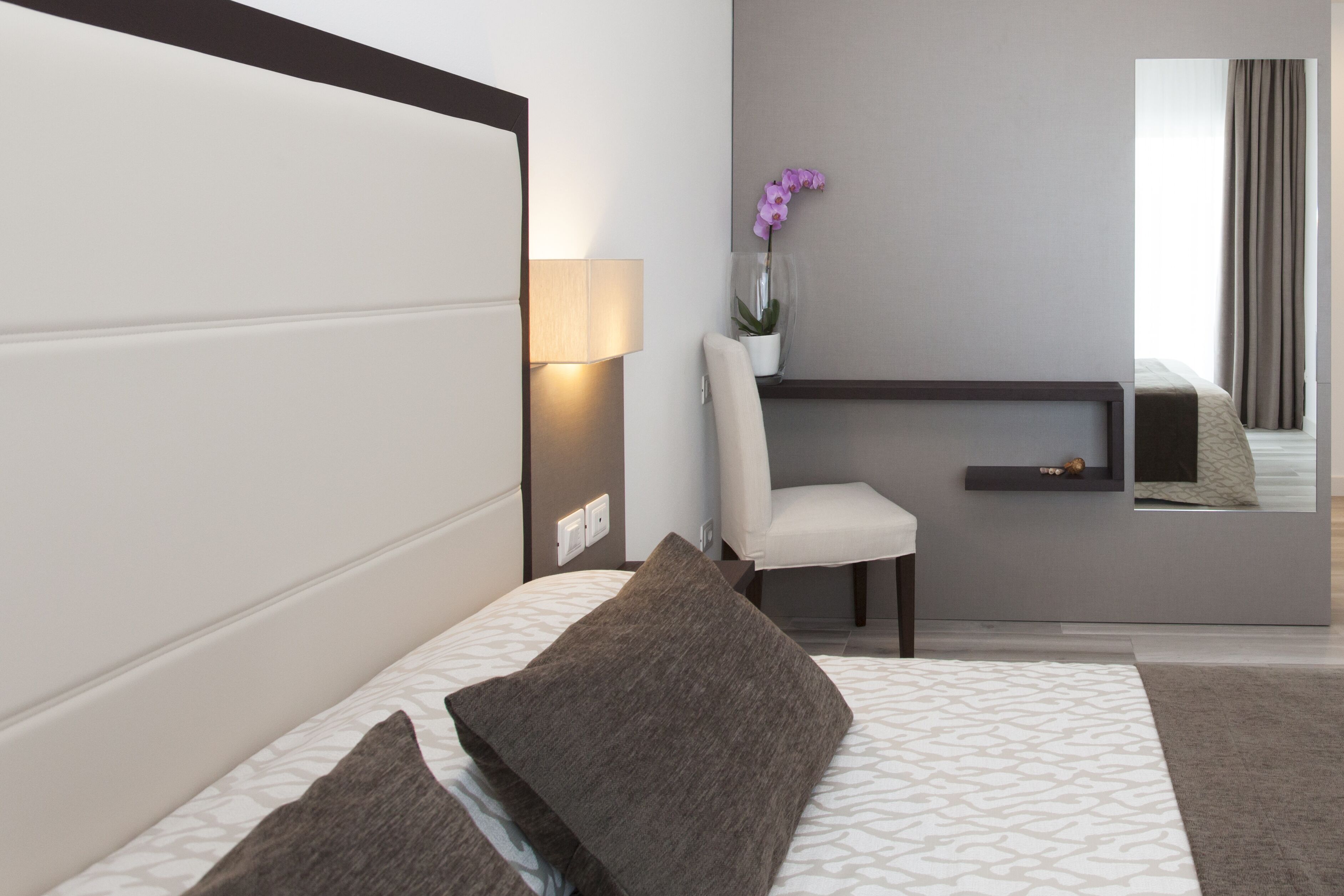 Ein modernes Hotelzimmer mit einem großen Bett, einem Nachttisch mit Lampe, einem Sessel, einem kleinen Schreibtisch und einer Topfpflanze.