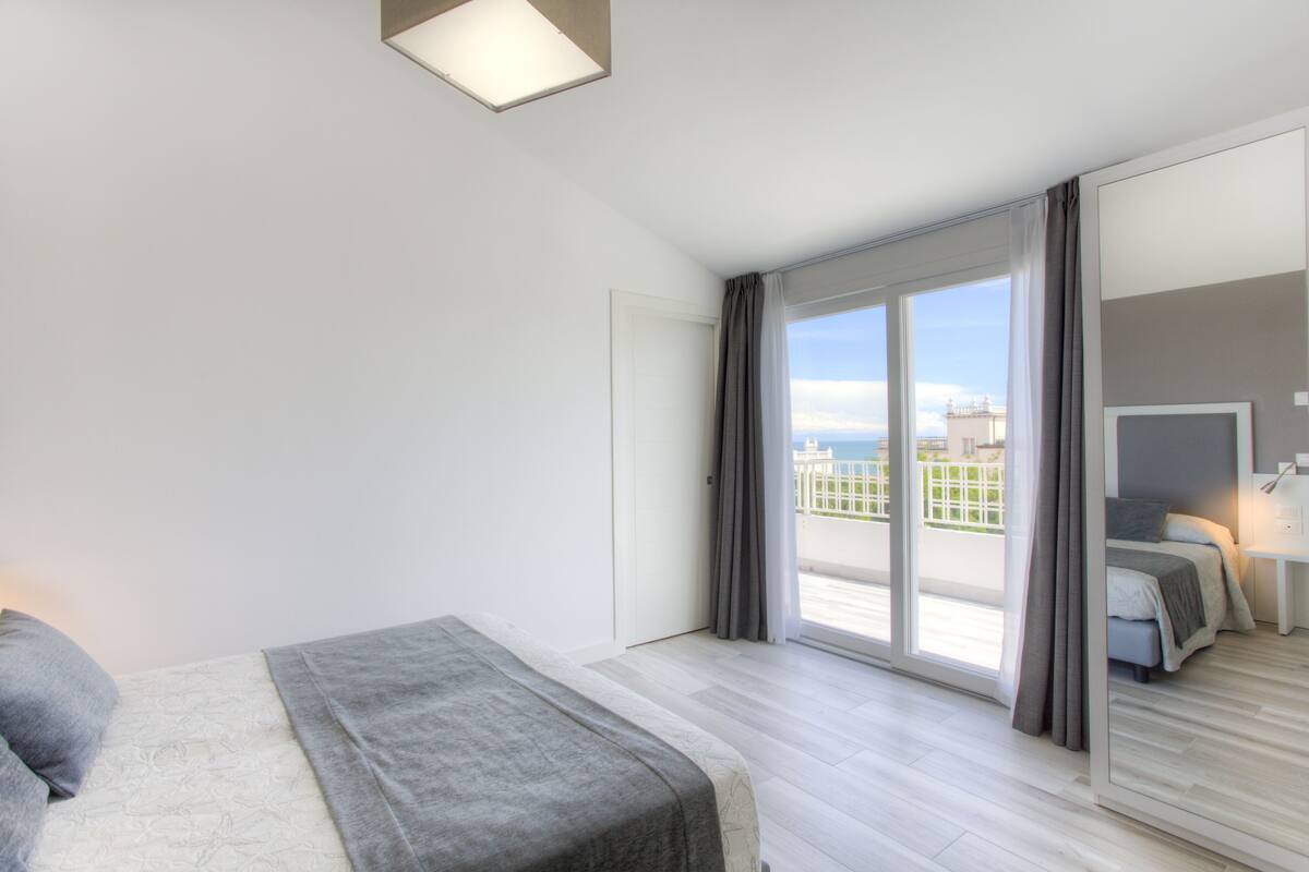 Una habitación de hotel moderna con una cama grande, un balcón con vistas a la ciudad y una puerta corrediza de vidrio.