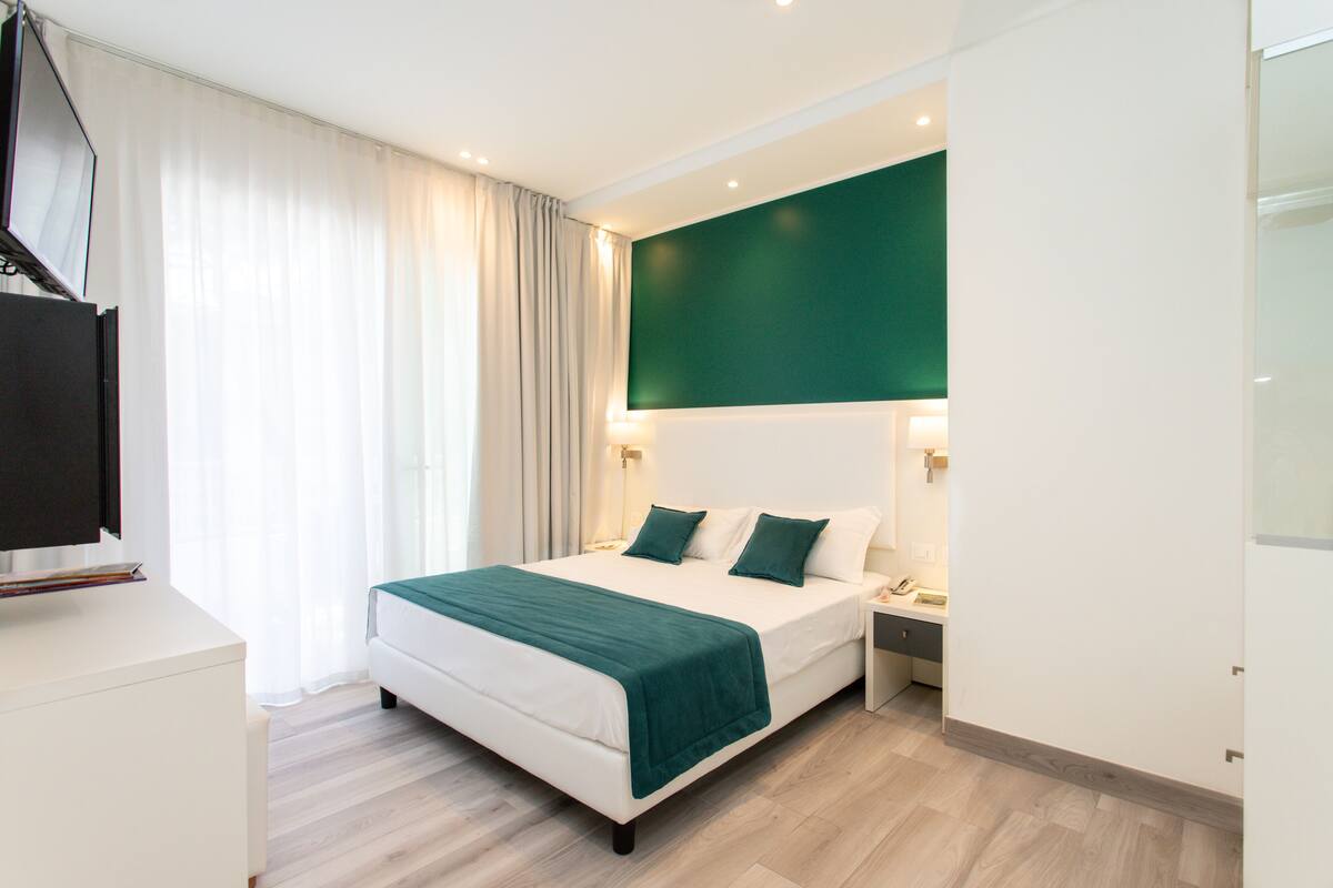 Habitación de hotel moderna con una cama grande, televisión de pantalla plana, mesita de noche y una pared de acento verde.