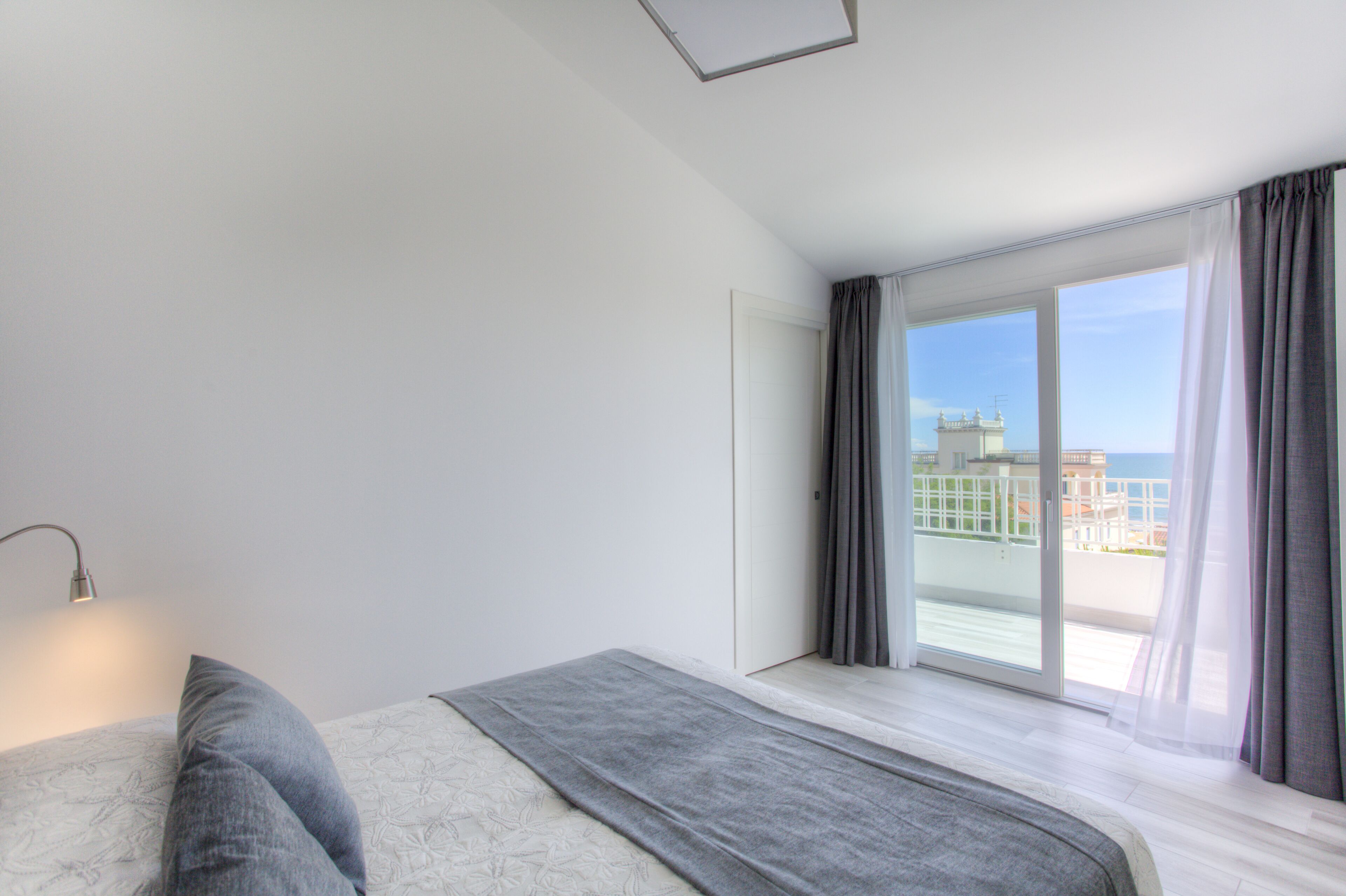 Een moderne hotelkamer met een groot bed, een bedlampje en uitzicht op de zee door een schuifglazen deur.