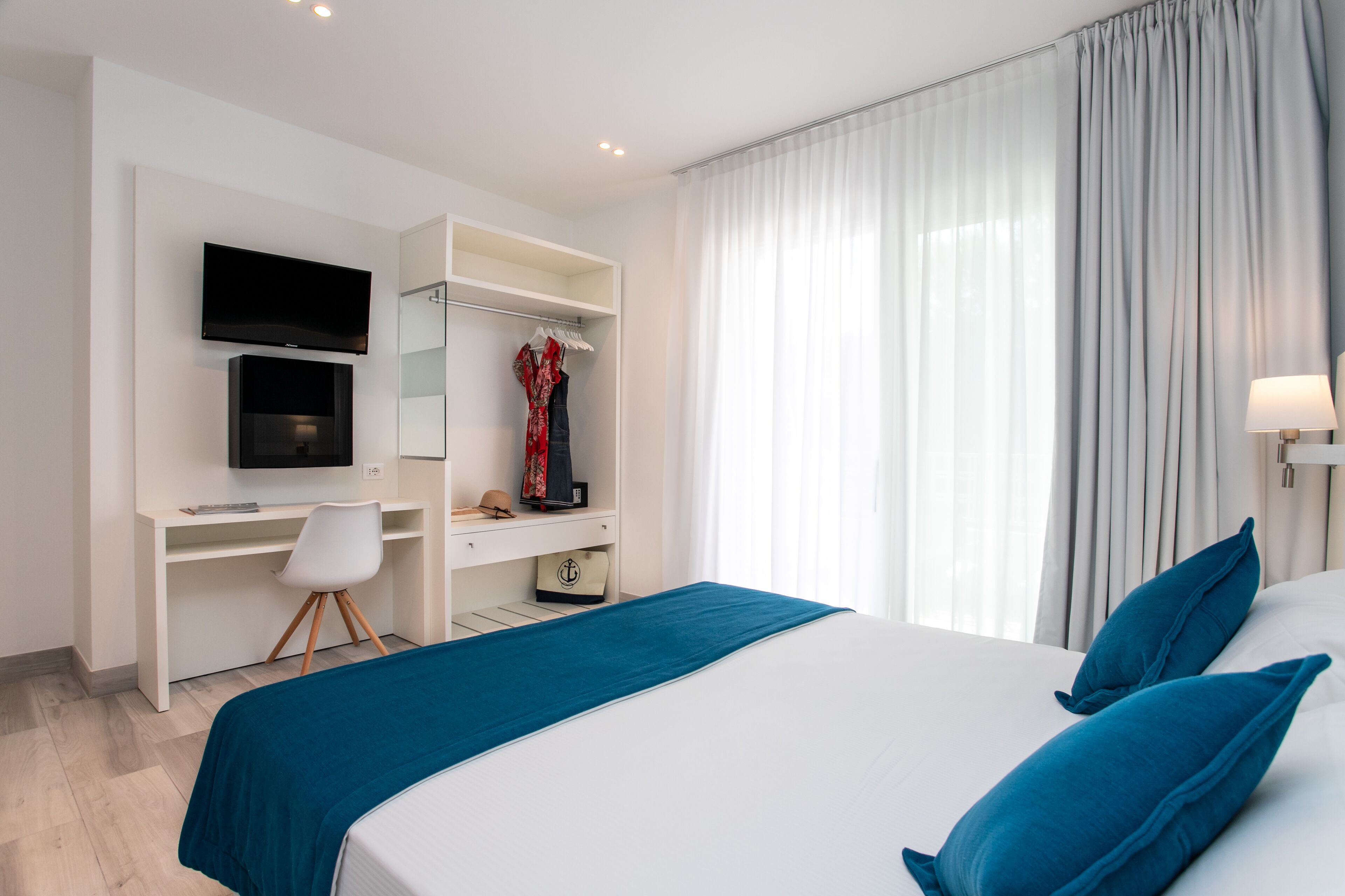 A hotel room with a bed, a desk with a TV, a wardrobe, and a window with curtains.