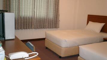 Ein Hotelzimmer mit zwei Betten, einem Schreibtisch mit Telefon und einem Fenster mit Vorhängen.