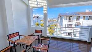 A balcony with a table and chairs, a view of buildings and a body of water. - Minh Duc Hotel (Tuan Chau)