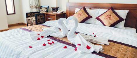 Una cama cuidadosamente tendida con una toalla con forma de cisne y pétalos de rosa, un cabecero de madera y dos almohadillas con un logotipo.
