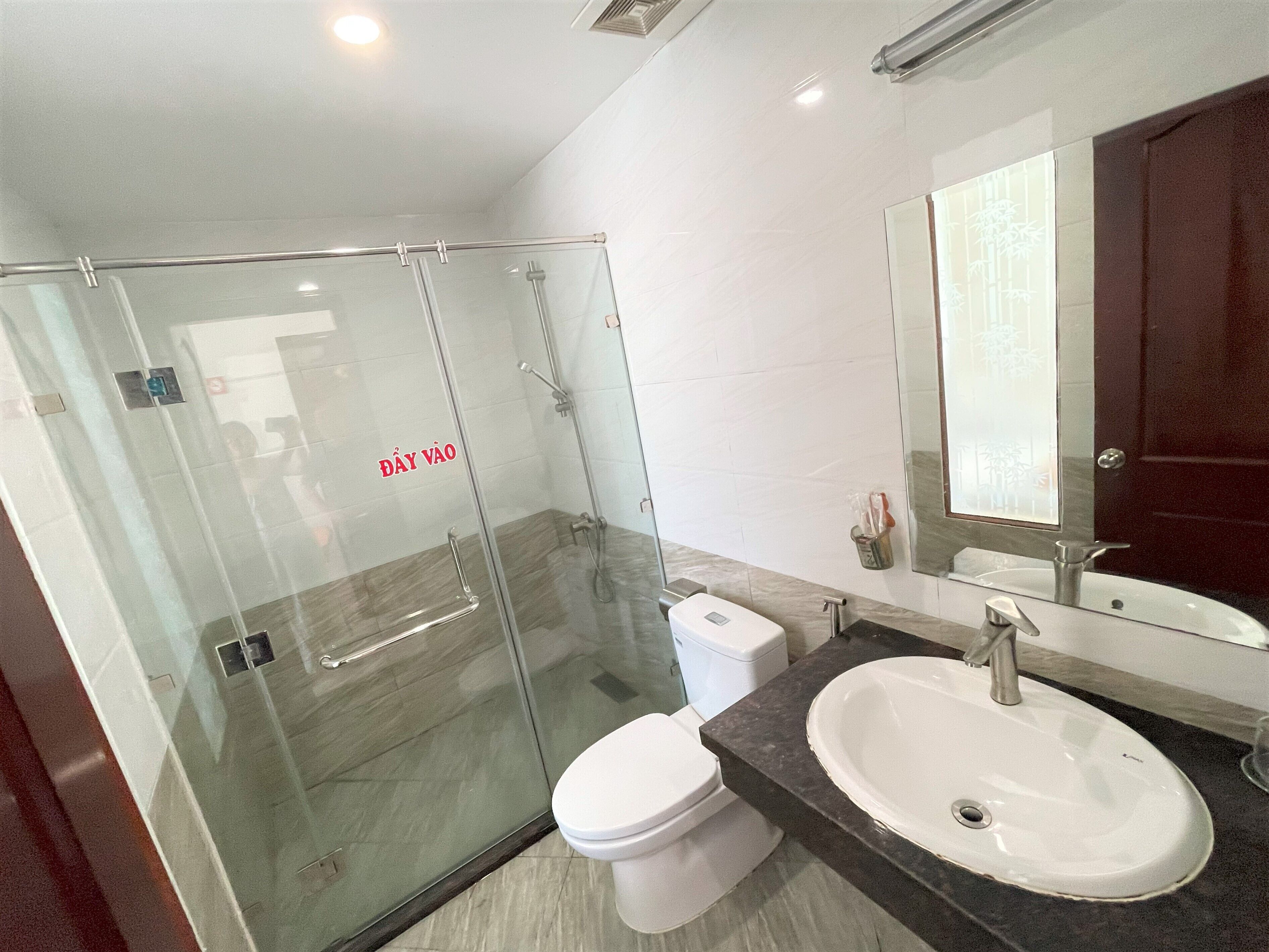 Une salle de bain moderne avec une douche à parois de verre, des toilettes blanches et un lavabo agrémenté d’un grand miroir.