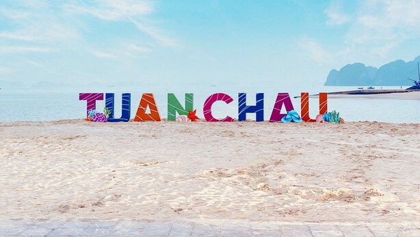 A beach with the word "TIANCHAU" spelled out in colorful letters, a sandy beach, and a calm sea with boats in the distance. - Minh Duc Hotel (Tuan Chau)