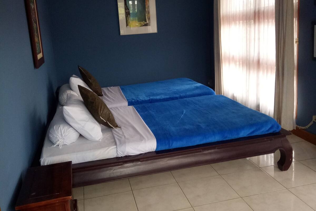 A bedroom with a bed, a small bedside table, a framed picture on the wall, and a window with curtains.