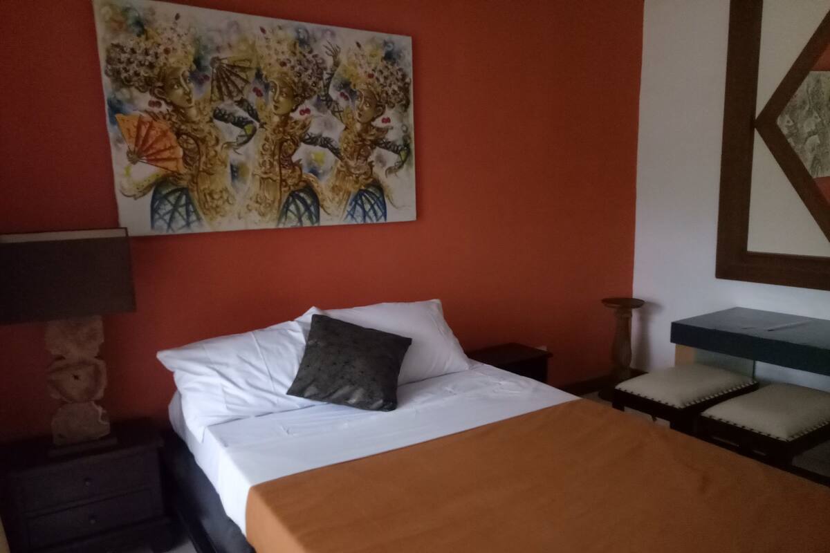 A hotel room with a bed, a nightstand, a lamp, a desk, and a chair.
