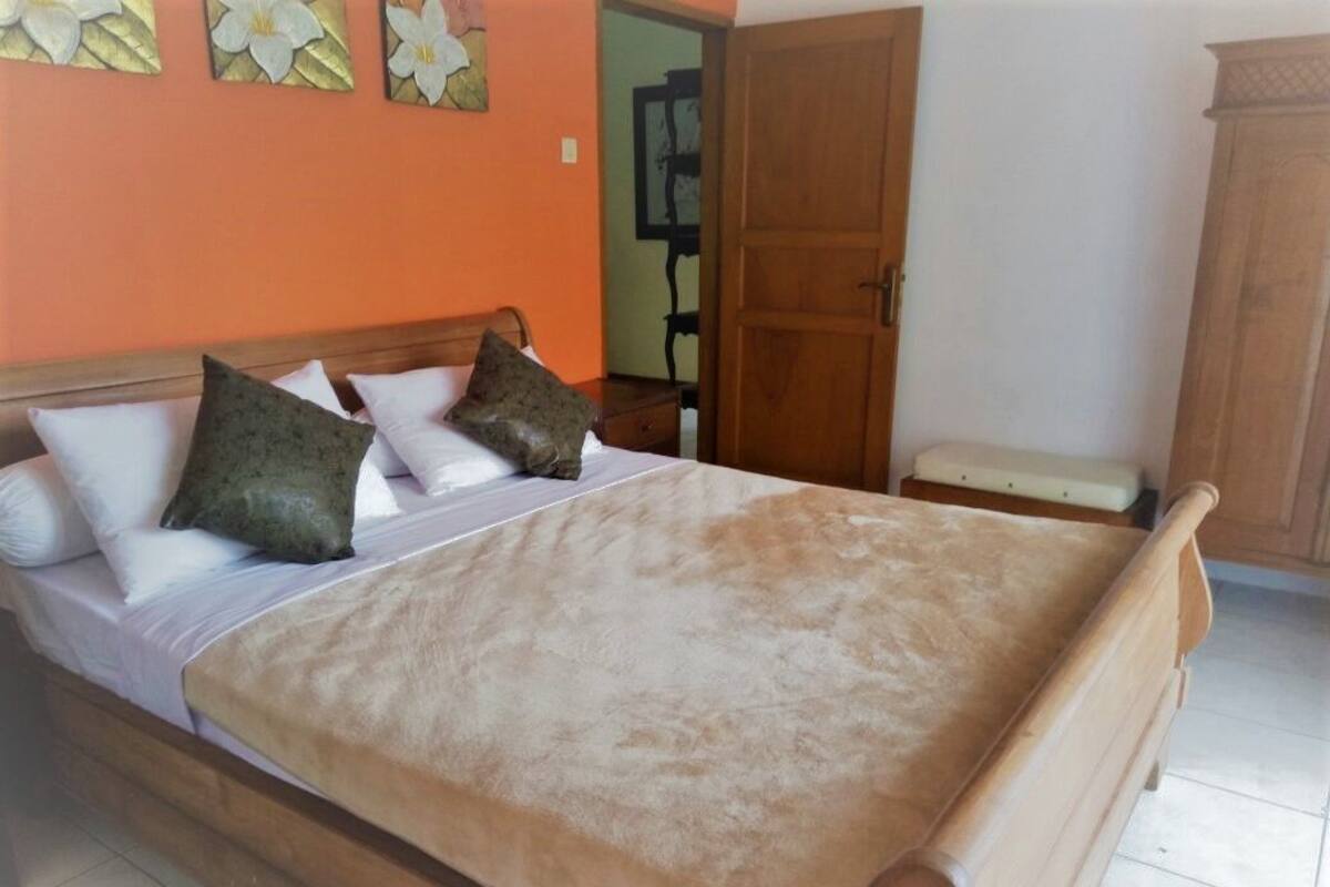 A bedroom with a wooden bed, white and green pillows, a beige blanket, and a wooden wardrobe.