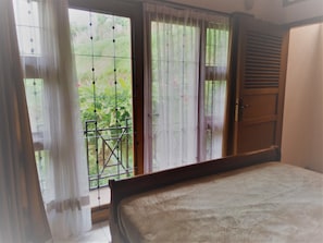 A bedroom with a bed, a window with curtains, and a view of greenery outside. - Kembang Guest House (Parongpong)
