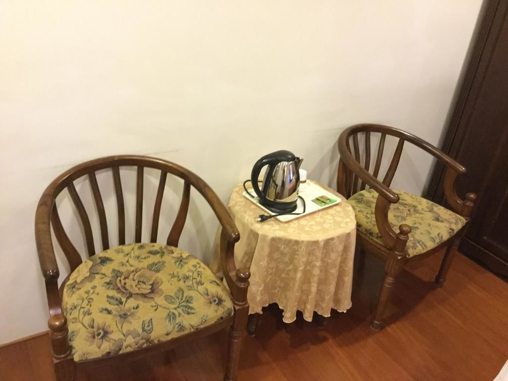 A small dining area with two wooden chairs and a table, featuring a floral-patterned cushion on one chair and a kettle on the table.