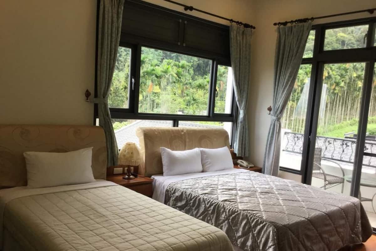 Une chambre d’hôtel avec deux lits, une grande fenêtre avec des rideaux et une vue sur la verdure.