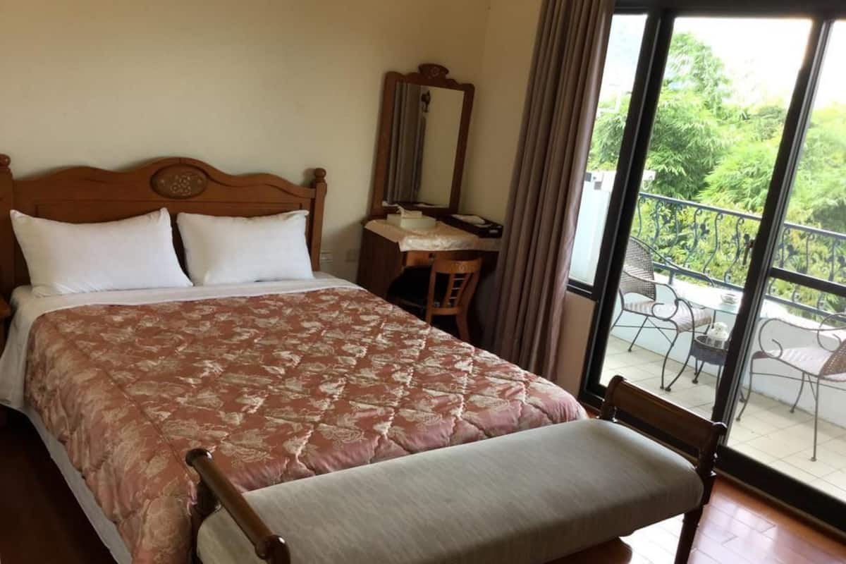 Une chambre avec un grand lit, un bureau en bois, une chaise et un balcon aménagé avec du mobilier d’extérieur.