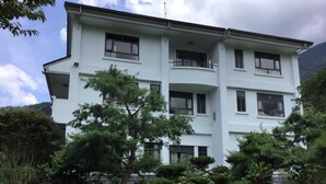 Un edificio de varios pisos con balcones, rodeado de follaje y árboles.