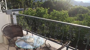 Un balcón con una mesa de vidrio y sillas de mimbre, con vistas a un exuberante paisaje verde.