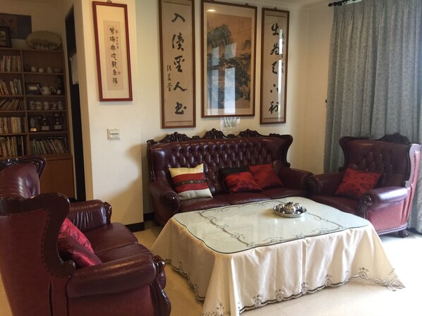 Un salon traditionnel avec un canapé en cuir, une table basse en verre et une bibliothèque remplie de livres et d’objets décoratifs.