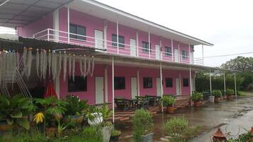 A pink building with a covered porch, outdoor seating, and potted plants.