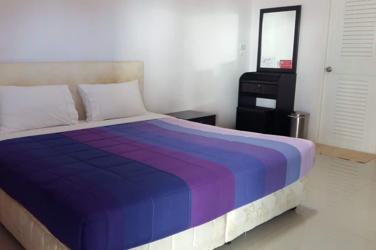 A hotel room with a bed, a nightstand, a black cabinet, and a mirror on the wall.