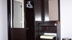 Un dormitorio con cama, armario, espejo, una pequeña estantería y un cubo de basura.