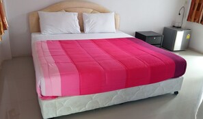 A bed with a white headboard, two white pillows, and a pink and white quilt. There is a small black nightstand with a silver appliance on it. - Bandung Grand (Ban Dung)