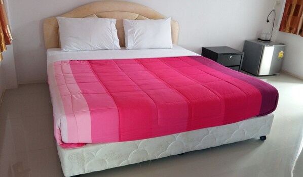 Una cama con cabecera blanca, dos almohadas blancas y colcha rosa y blanca. Hay una mesita de noche negra con un electrodoméstico plateado encima.