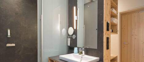 A modern bathroom with a large mirror, a white sink, and a wooden vanity.